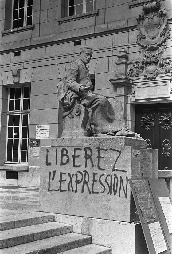 Black-and-white photograph of a statue's stone base at the Sorbonne painted with the slogan "Libérez l'expression."