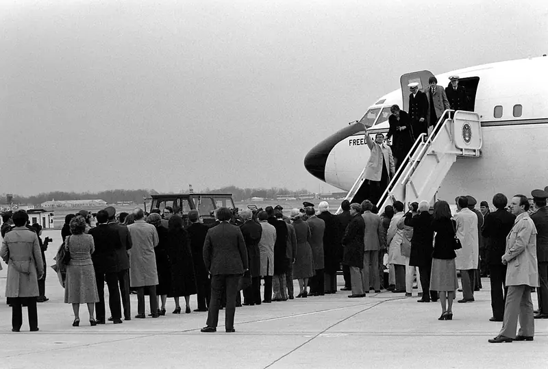 Black-and-white photo of a crowd on an airport tarmac watching people step down the stairs of a white government jet marked "Freedom One."